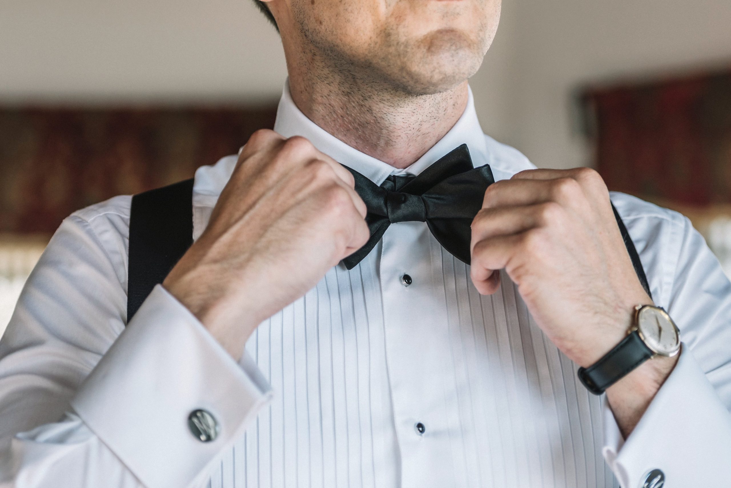 Groom straightening a black bowtie on a pleated white dress shirt